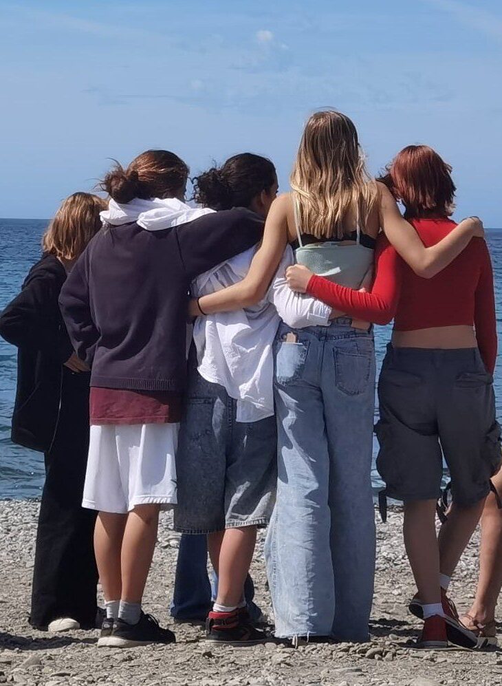 Group of teenage girls standing in front of sea with arms around eachother