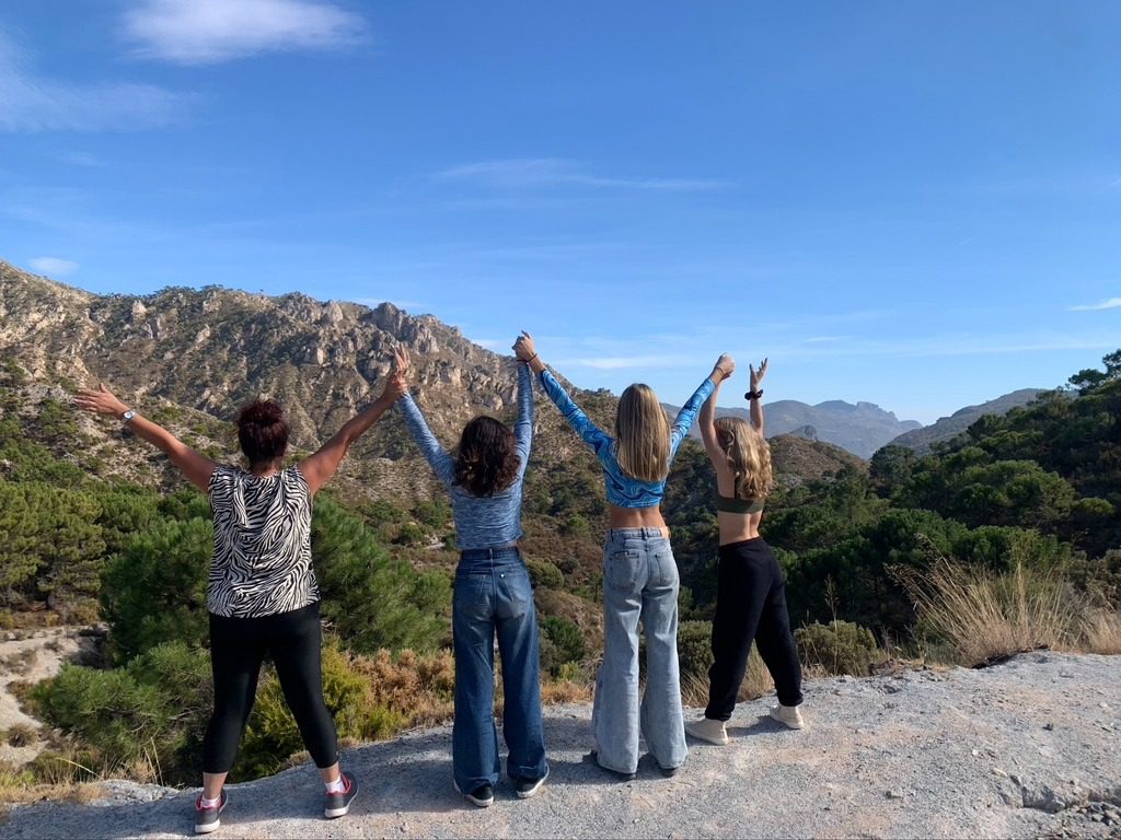 Four young women with outstretched arms looking at mountains